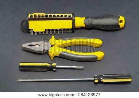 A Set Of Tools On A Gray Background Pliers, Screwdriver, Insulating Tape, Saw.