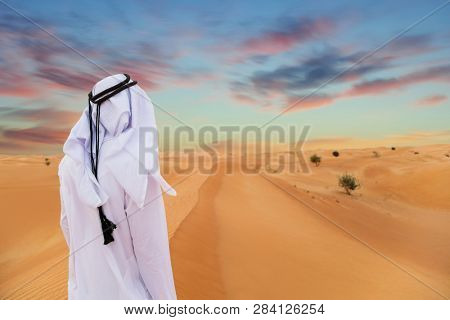Arabic man with traditional emirates clothes in the desert, sunset.