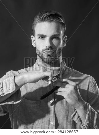 Hairdresser In Denim Shirt Demonstrating Sharp Blade Of His Dangerous Razor. Man With Beard And Must