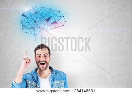 Portrait Of Happy Young Man In Jeans Shirt Standing With Open Mouth And Finger Pointing Up Near Conc
