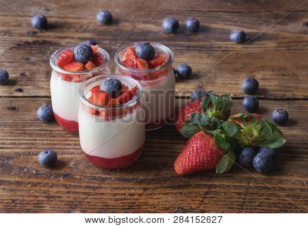 Delicious Homemade Yogurt With Strawberry Jam And Sliced Strawberries And Blueberries, On A Wooden B