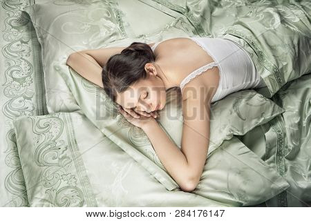 Beautiful young woman sleeping in luxury bed. Bed is made with linen embroidered percale.