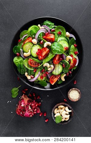 Spinach Salad With Fresh Cucumbers, Tomato, Onion, Pomegranate, Sesame Seeds And Cashew Nuts On Blac