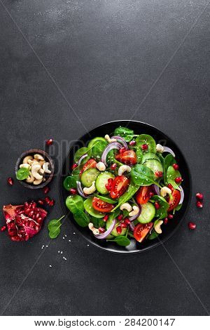 Spinach Salad With Fresh Cucumbers, Tomato, Onion, Pomegranate, Sesame Seeds And Cashew Nuts On Blac