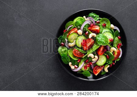 Spinach Salad With Fresh Cucumbers, Tomato, Onion, Pomegranate, Sesame Seeds And Cashew Nuts On Blac
