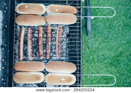 Top View Of Tasty Hot Dogs Grilling On Bbq Grill Grade On Green Grass Background