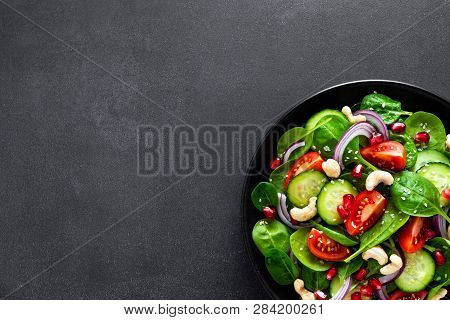 Spinach Salad With Fresh Cucumbers, Tomato, Onion, Pomegranate, Sesame Seeds And Cashew Nuts On Blac