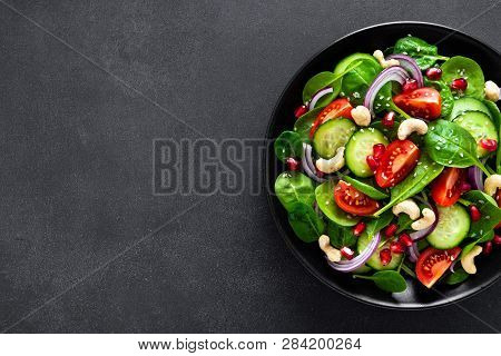 Spinach Salad With Fresh Cucumbers, Tomato, Onion, Pomegranate, Sesame Seeds And Cashew Nuts On Blac