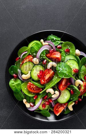 Spinach Salad With Fresh Cucumbers, Tomato, Onion, Pomegranate, Sesame Seeds And Cashew Nuts On Blac