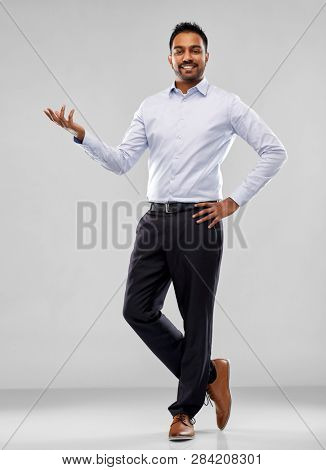 business, office worker and people concept - happy indian businessman holding something imaginary over grey background