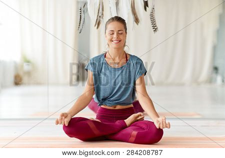 mindfulness, spirituality and healthy lifestyle concept - woman meditating in lotus pose at yoga studio