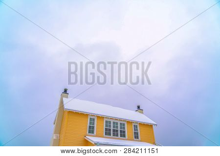 Yellow House With Snow Covered Roof Against Sky