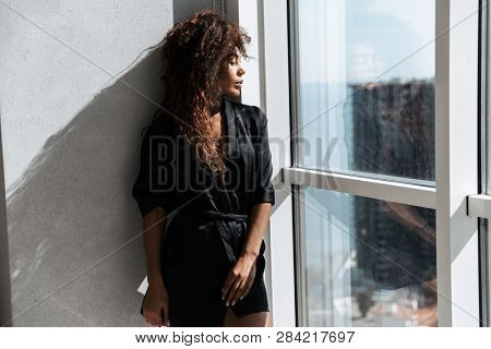 Portrait of brunette african american woman wearing housecoat standing near window indoor