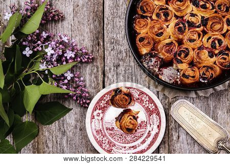 Homemade Mini Cherry Rolls In A Baking Form And Two Rolls On A Plate With Bouquet Of Lilac On Vintag
