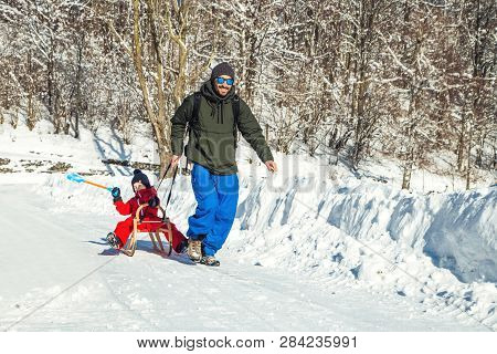 Happy Father And His Son Enjoying Sledding Ride. Happy Family With Sled In Winter Having Fun Togethe