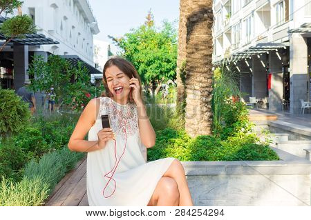 Beautiful Brownhair Woman Is Listening Music In Headphones In The Park. She Is Wearing Fashionable W