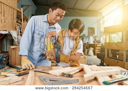 Preteen Vietnamese Boy Drilling Wooden Plancks In Workshop Under Control Of His Father