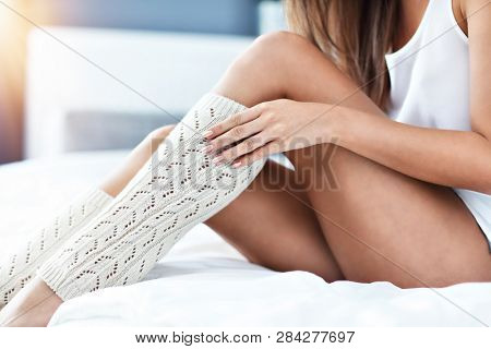 Young woman putting on warmers in bed