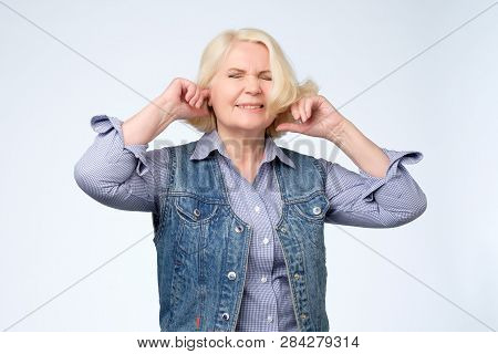 Unhappy Stressed Out Senior Female Making Wry Face, Plugging Ears With Fingers