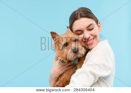 Cheerful young woman standing isolated over blue backgroundm hugging a dog