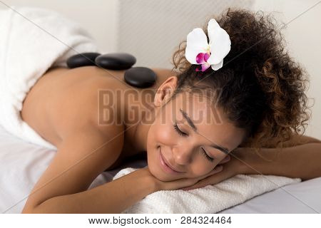Woman Enjoying Hot Stone Massage At Spa Salon With Closed Eyes