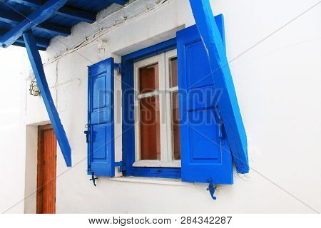 Window In Mykonos, Greece With Traditional Paint Colors Of Blue Shutters And Awning And Red Door On 