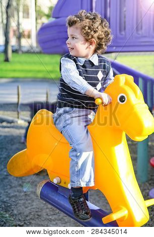 Three Year Old Baby Is Swinging On A Cockhorse On The Playground.