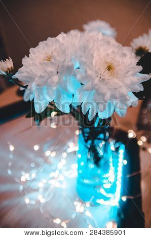 Lights Shining Behind The Bouquet Of White Fresh Flowers. Top View On The Decoreted Wooden Table.