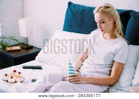 Uspet Woman Holding Party Hat While Celebrating Birthday In Bed Alone