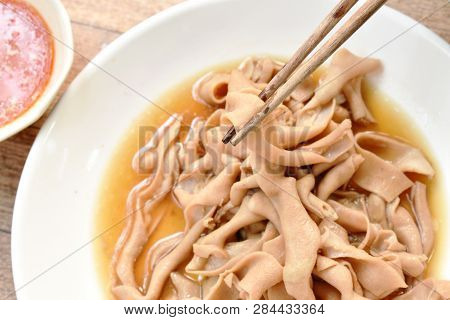 Wooden Chopsticks Picking Stewed Duck Intestine In Brown Soy Soup Dipping Spicy Sauce