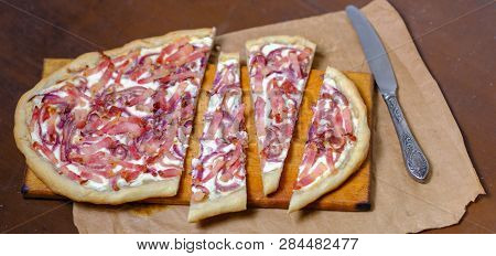 Alsatian Tart Flambé Or Flammkuchen With Bacon And Onions On A Dark Table.