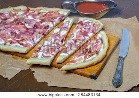 Alsatian Tart Flambé Or Flammkuchen With Bacon And Onions On A Dark Table.