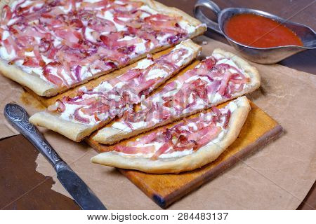 Alsatian Tart Flambé Or Flammkuchen With Bacon And Onions On A Dark Table.