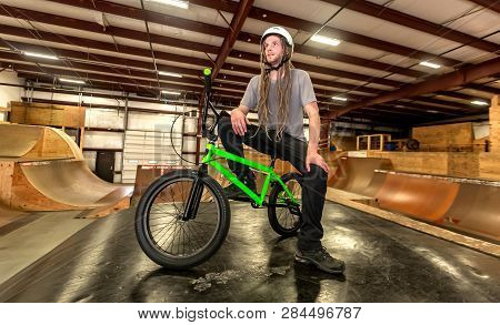 Portrait Of A Man With Dredlocks And A Helmet On A Bmx Bike At An Extreme Sports Park