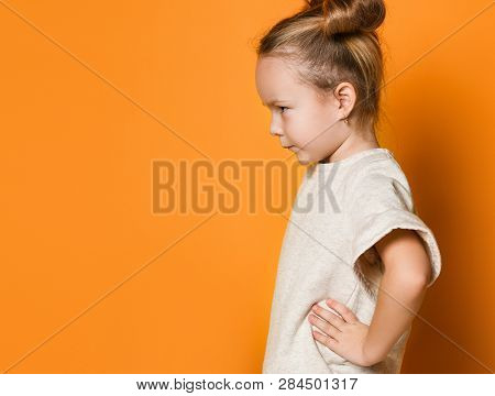 Little Cute Girl In A Light Dress Looks Away Angrily, Her Arms Are In Sides. On Yellow Background, S
