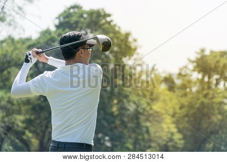 The Back Of Golf Player In White Shirt Swinging Glof. Young Man Practicing His Swing On The Golf Cou