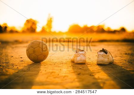Old Soccer Football And Shoes On The Dirt Field.
