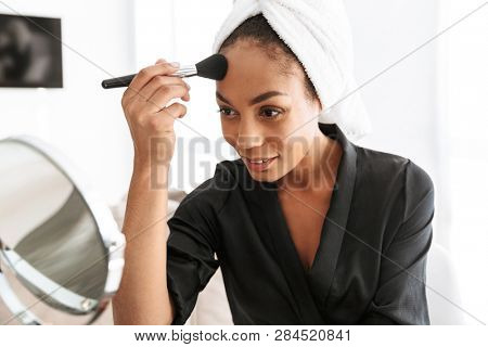 Portrait of adorable african american woman in housecoat wrapped in white towel applying makeup at home