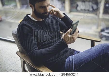 Cheerful Hispanic Bearded Man In Black Pullover Using Mobile Phone Application For Mobile Blogging. 