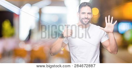 Young man wearing casual white t-shirt over isolated background showing and pointing up with fingers number six while smiling confident and happy.