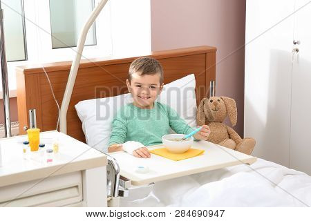Little Child With Intravenous Drip Eating Soup In Hospital Bed