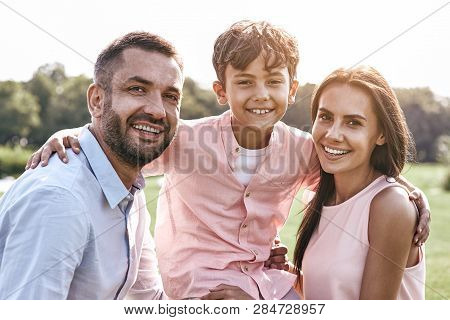 Bonding. Family Of Three Walking On Grassy Field Son Hugging Par