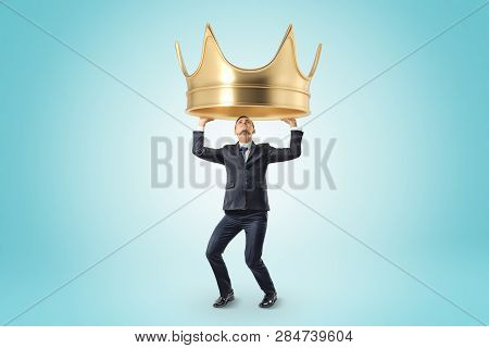 Young Businessman Holding Heady Golden Crown Above Head On Blue Background