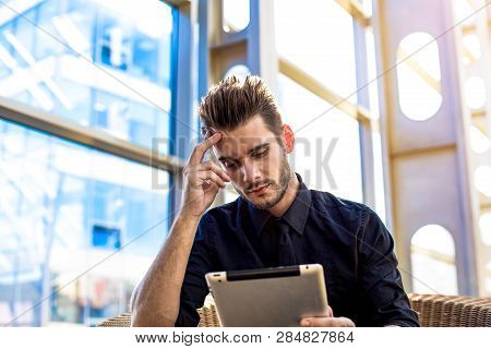 Thoughtful Male Economist Reading Financial News On Portable Touch Pad Computer, Sitting In Airport 