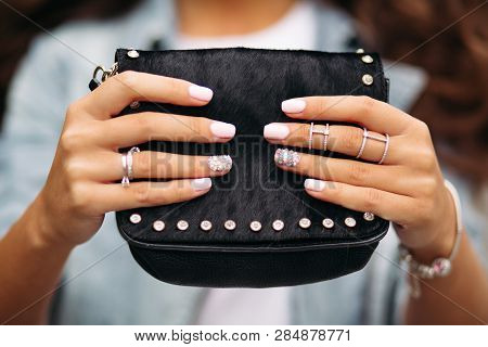 Girl With Manicured Nails With Beautiful Ornament In Wedding Rings Holding Black Fur Bag.