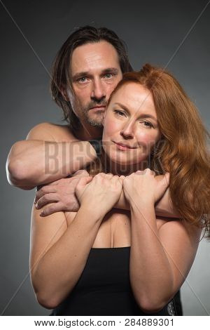 Portrait Of Beautiful Calm Woman In Bare Shoulder Dress Being Embraced By Her Topless Thoughtful Hus