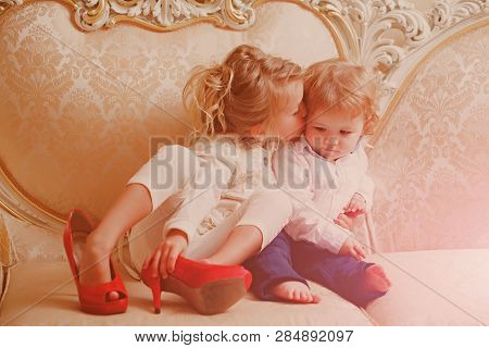 Girl Kiss Boy With Blond Hair On Classic Sofa. Family, Love, Trust Concept. Kid Beauty, Look. Fashio