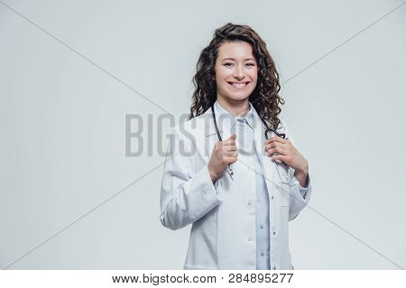 A Serious Young Woman In A Caucasian Woman In A Laboratory Robe, Looking At You And Holding The Phon