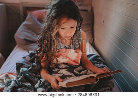 Thoughtful Kid Girl Reading Book Alone In Her Room In The Veening Or Early Morning