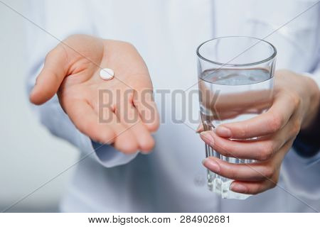 A Young Girl Doctor Takes Vitamins. At The Same Time, She Stands On A Gray Background Dressed In A W
